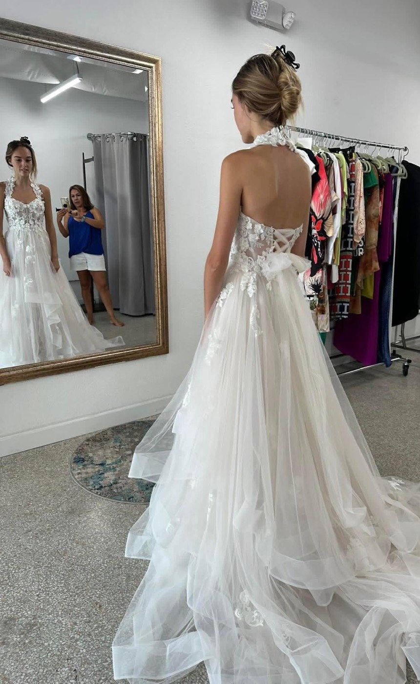 Back of a halter-neck wedding gown with a lace-up back and a layered tulle skirt, reflected in a large gold-framed mirror
