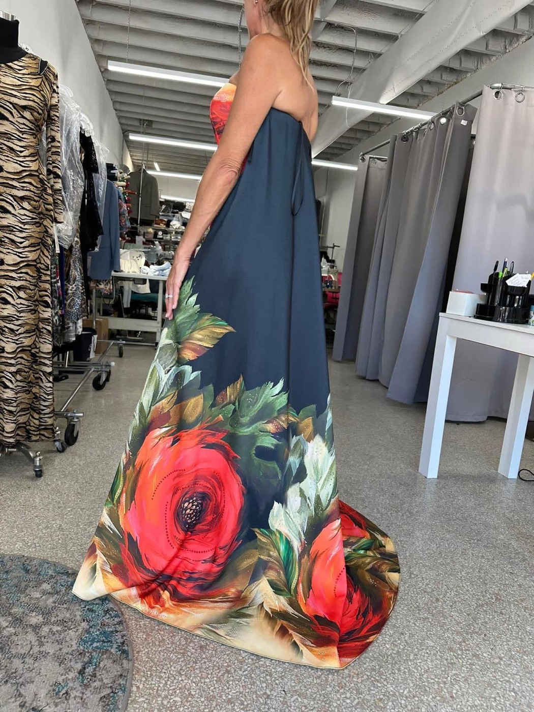 Side view of a strapless navy gown with a large red rose print at the hem, in the fitting room