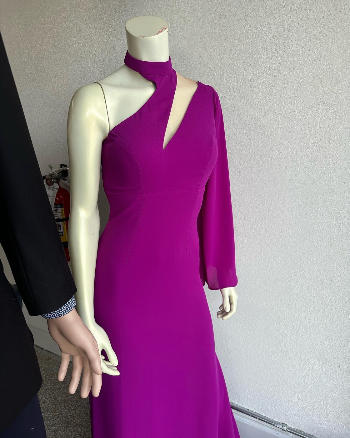 Mannequin in a purple one-shoulder gown with a high collar and a cutout, next to a mannequin in a dark suit jacket