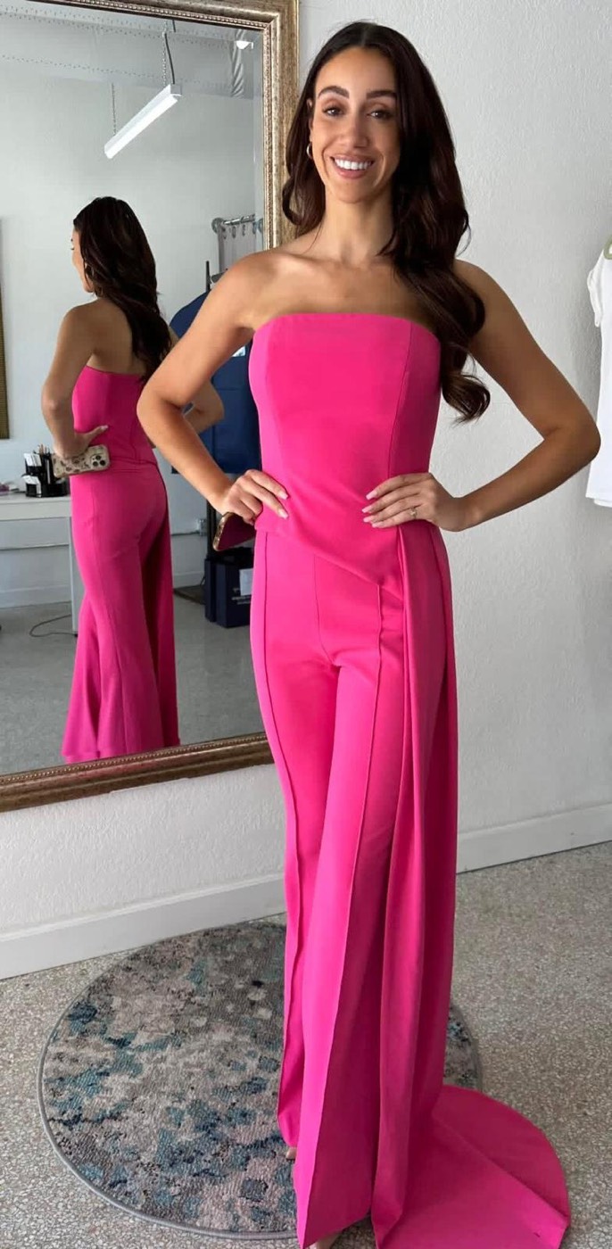 Woman in a strapless hot-pink jumpsuit with wide legs and a draped train, in front of the fitting mirror